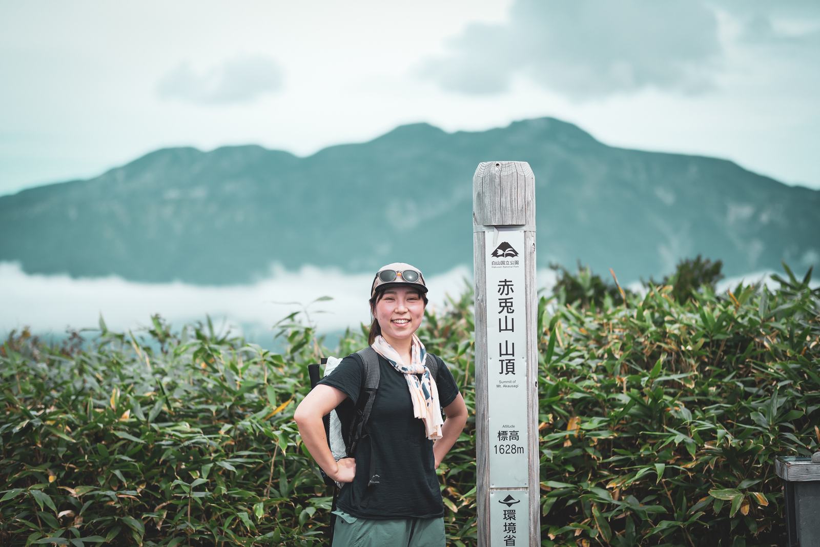 赤兎山の山頂標識の横で笑う人