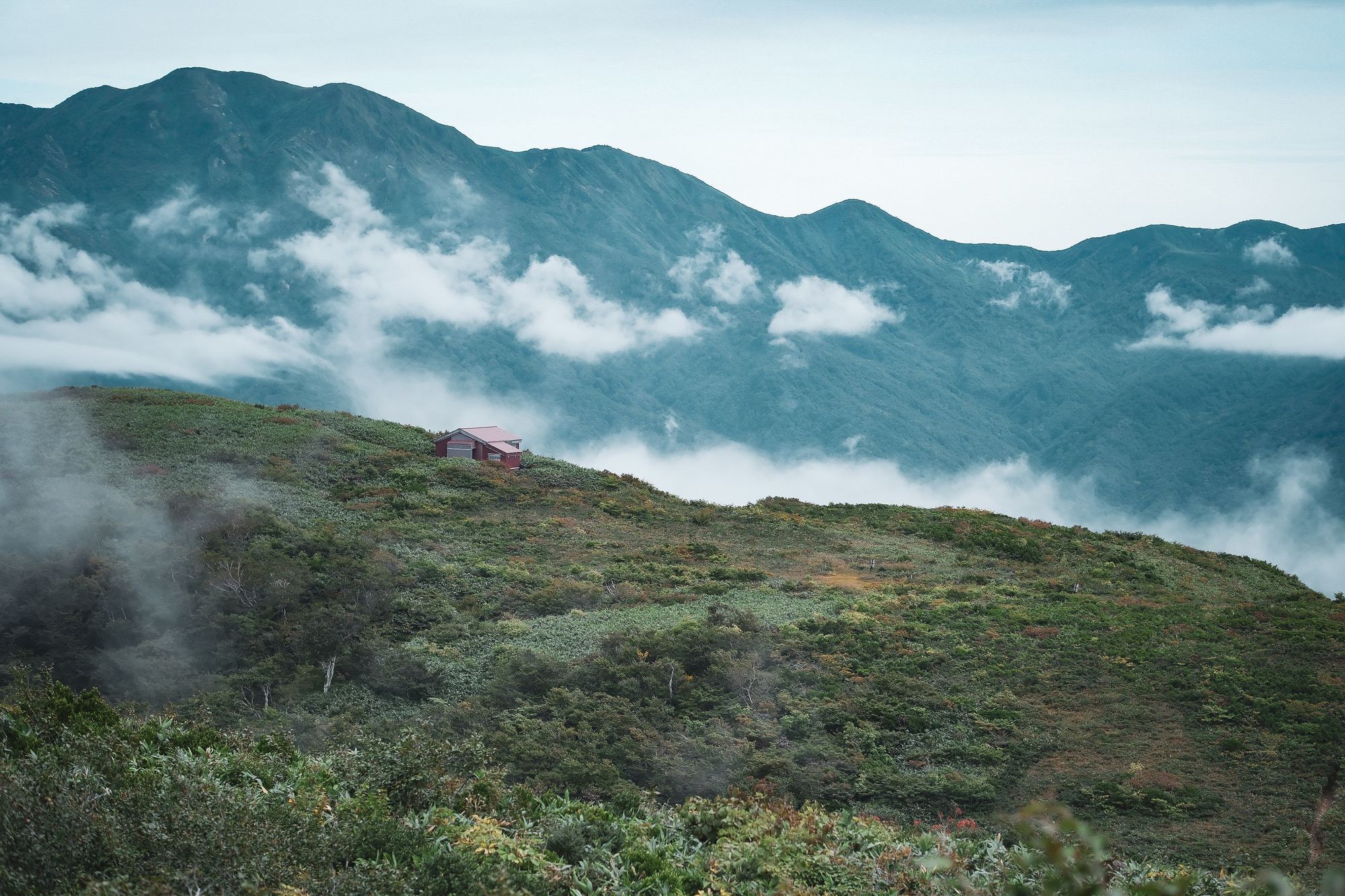 雲が流れる稜線と、草原の登山道